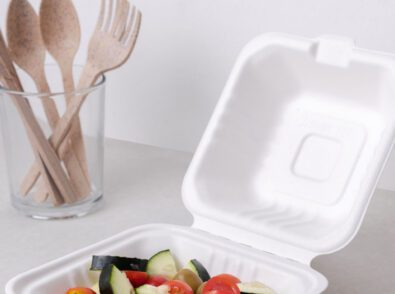 a styrofoam container filled with vegetables next to a glass of wooden utensils